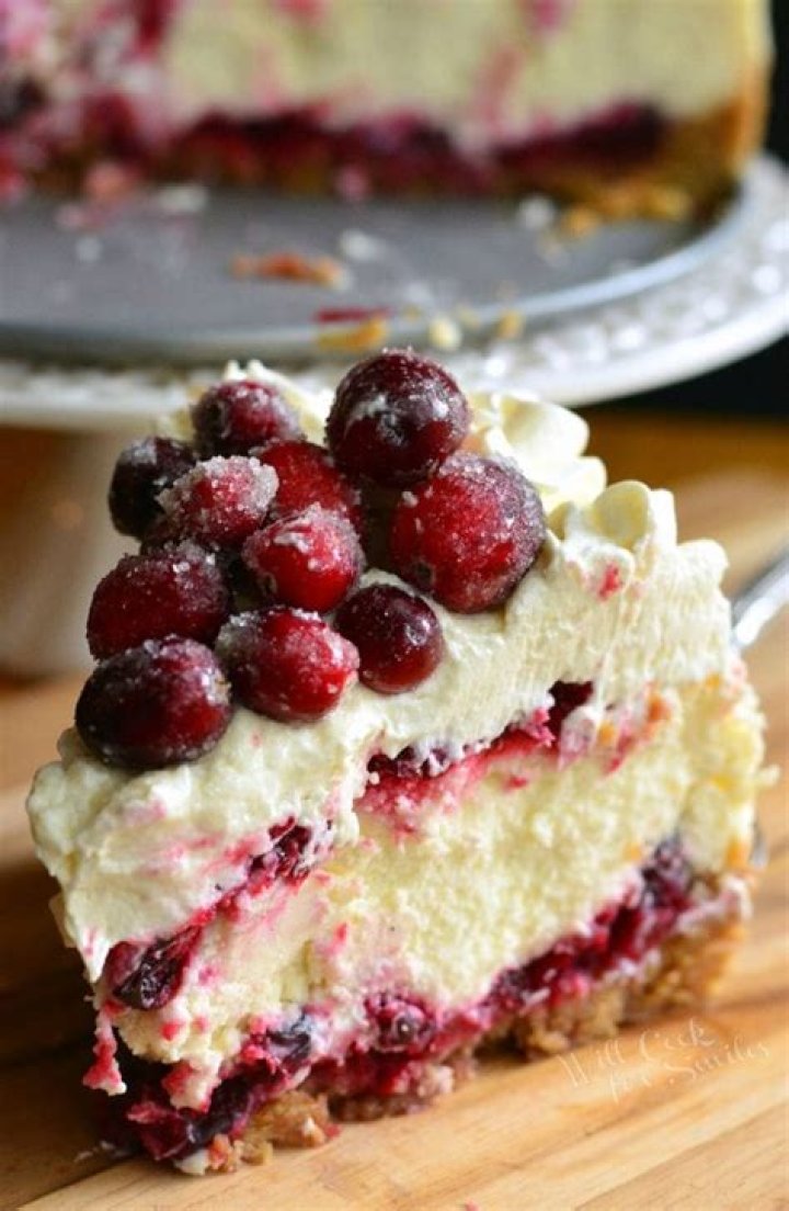 White chocolate cranberry cheesecake decorated with white chocolate shavings, whipped cream, and fresh cranberries.
